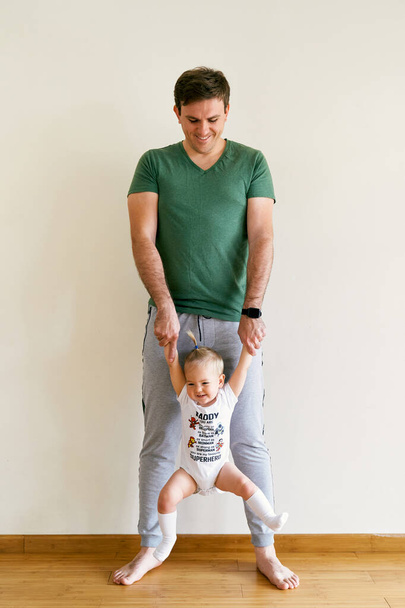 Smiling dad holds the hands of a little girl while standing on the floor of the room - Foto, Imagem
