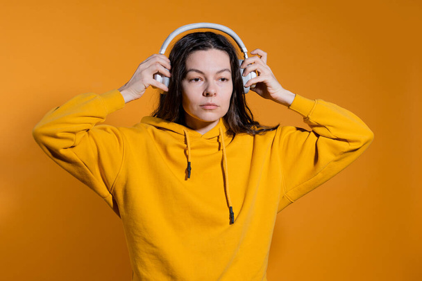 Music lovers enjoy music. A young woman in a yellow hoodie with white wireless headphones, - Zdjęcie, obraz