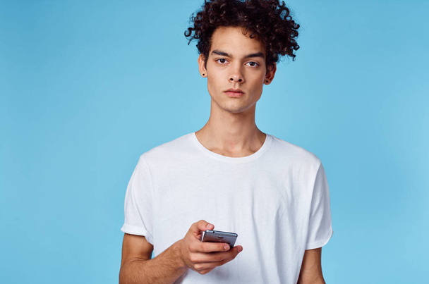 guy in white t-shirt curly hair phone in hands technology blue background - 写真・画像