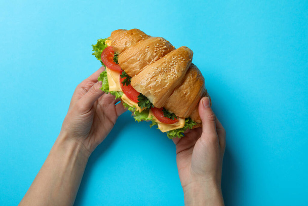 Γυναικεία χέρια κρατούν κρουασάν σάντουιτς σε μπλε φόντο - Φωτογραφία, εικόνα