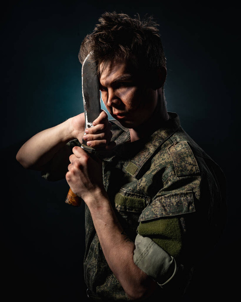 Πορτρέτο ενός στρατιώτη με ουλές και χρωματισμό μάχης, κρατώντας μια μαχαίρα σε μαύρο φόντο - Φωτογραφία, εικόνα