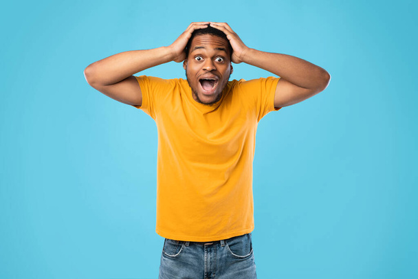 Megdöbbent afro-amerikai srác kiabálva Érintés fej felett kék háttér - Fotó, kép