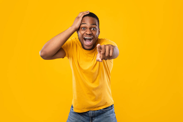opgewonden Afrikaanse man wijzend vinger op camera lachen, gele achtergrond - Foto, afbeelding