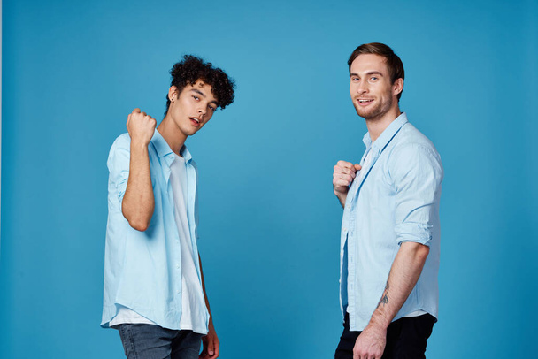 krullenbol kerel in een shirt groet zijn vriend op een blauwe achtergrond - Foto, afbeelding
