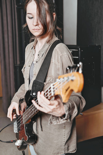 young woman wearing casual clothes and playing electric bass guitar. female bass guitarist standing in a rehearsal room - Photo, Image