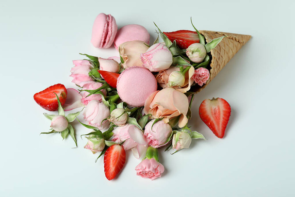 Vaflovací kornout s květinami, jahodami a makaróny na bílém pozadí - Fotografie, Obrázek