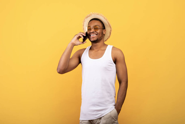 Feliz hombre negro en ropa de verano haciendo llamada en el teléfono celular, tener conversación sobre fondo amarillo estudio - Foto, Imagen