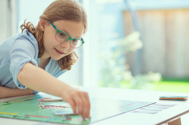 Portrait of pretty teen girl in glasses playing board game with parents at home - Valokuva, kuva