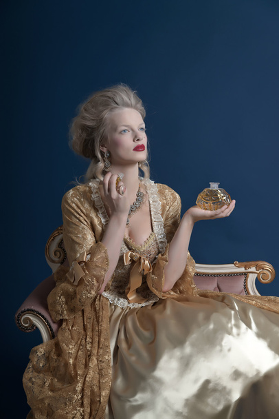 Retro baroque fashion woman wearing gold dress. Holding bottle o - Фото, зображення
