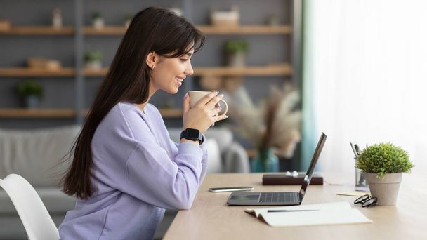 Mujer sonriente viendo vídeo en la computadora, bebiendo café - Foto, Imagen