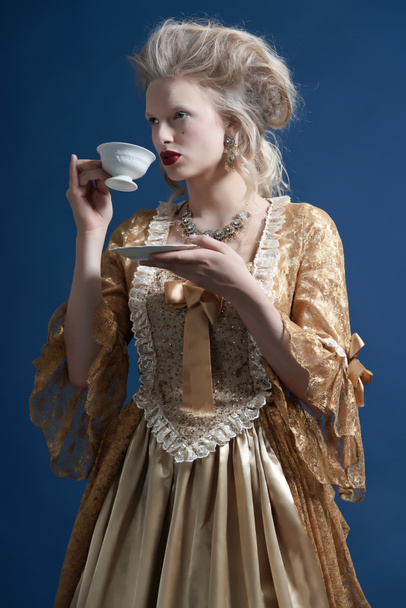 Retro baroque fashion woman wearing gold dress. Holding a cup of - Photo, Image