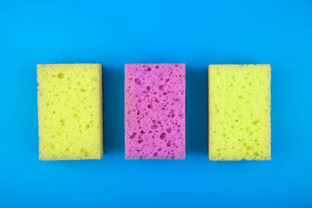 Yellow and purple sponges for house cleaning and dish washing on blue background - Foto, afbeelding