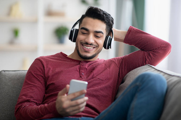 Hombre árabe positivo viendo películas en línea, utilizando el teléfono móvil - Foto, Imagen