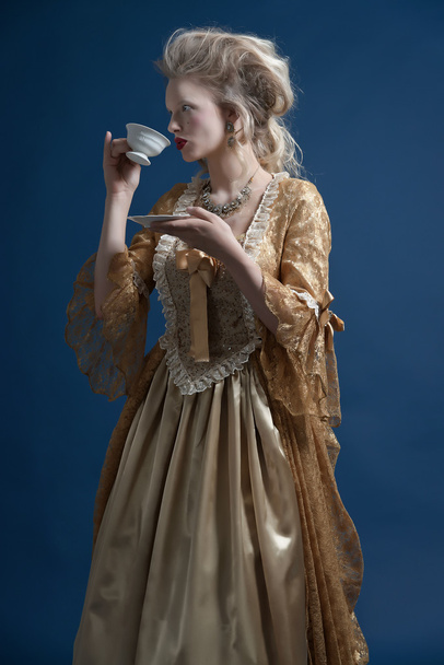 Retro barocco donna di moda indossa abito d'oro. Con in mano una tazza di
 - Foto, immagini