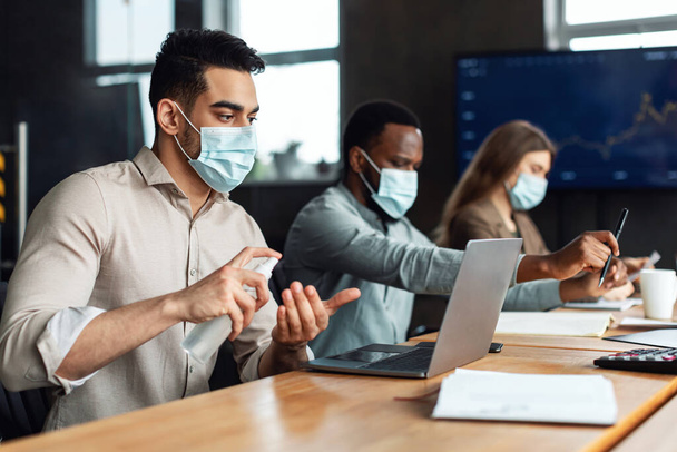 Internationale Kollegen tragen medizinische Masken mit Desinfektionsmittel an den Händen - Foto, Bild