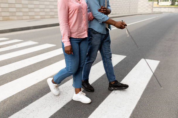 Vista ritagliata di badante femminile che assiste l'uomo di colore ipovedente con canna attraversare la strada della città, primo piano - Foto, immagini