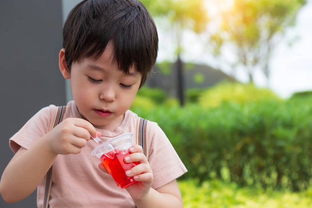 A un niño pequeño y lindo le encanta comer dulces o bocadillos. Niño guapo disfrutar de comer gelatina o gelatina. Adorable chico como comer bocadillos. Se siente feliz cuando come dulce favorito con fondo de jardín - Foto, imagen