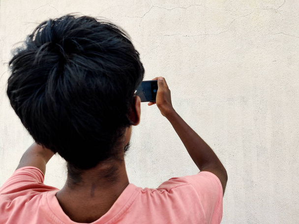 Вид сзади на молодого человека, фотографирующего белую стену на мобильный телефон. - Фото, изображение