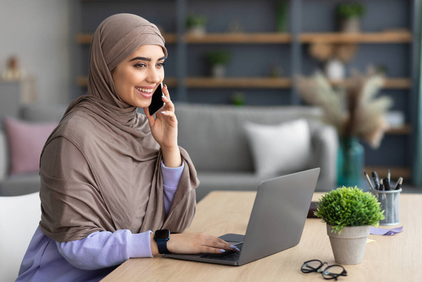 Femme musulmane souriante qui travaille et parle au téléphone à la maison - Photo, image
