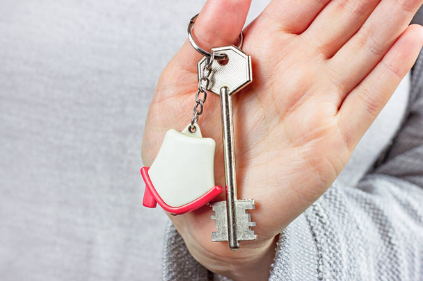 Fehér nő fogja a kulcstartót a kulcsokkal és a kis ház kulcscsomójával. Lakásbérlő, ingatlan tulajdon, ingatlan vásárlási koncepció. - Fotó, kép