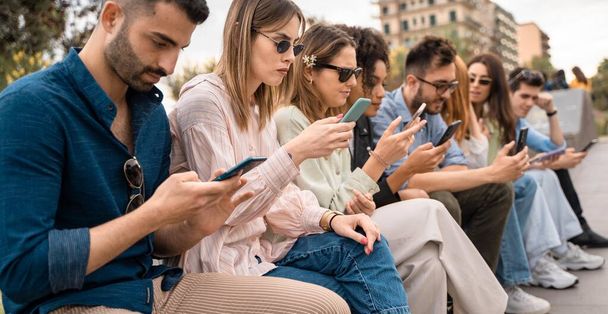 Group of young people surfing the internet watching social network contents sitting outdoors. Friends addicted from smartphones and people using tech concept. - Photo, Image