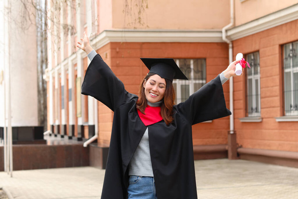 Szczęśliwa studentka w kawalerskim szlafroku i z dyplomem w dniu ukończenia szkoły - Zdjęcie, obraz