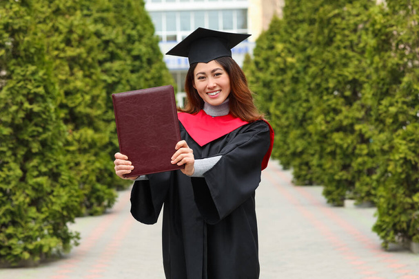 Studentin im Bachelor-Gewand und mit Buch am Abschlusstag - Foto, Bild
