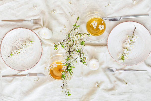 Table setting with blooming branches and cups of tea on light background - Фото, изображение