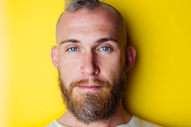 Πορτρέτο του μπλε μάτια γενειοφόρος βάναυση άνθρωπος σε κίτρινο φόντο - Φωτογραφία, εικόνα