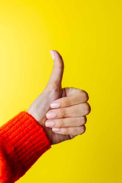 Woman's hand in red sweater shows thumb up on yellow background - Valokuva, kuva