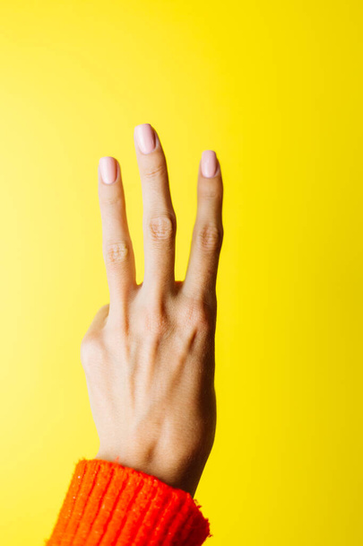 Ręka kobiety w czerwonym swetrze pokazuje trzy palce na żółtym tle - Zdjęcie, obraz