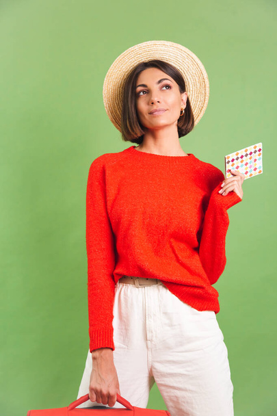 Woman in red casual sweater on green background in straw hat hold suitcase going to vacation cheerful happy excited think where to fly - Valokuva, kuva