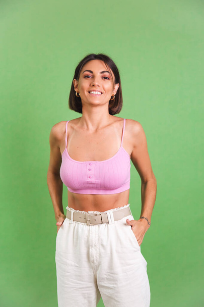 Woman in pink crop top and white trousers on green background stylish fit good shape happy positive excited cheerful posing - Foto, afbeelding