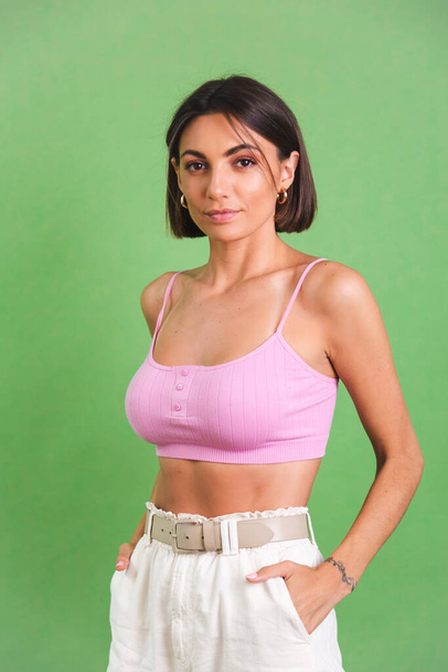 Woman in pink crop top and white trousers on green background stylish fit good shape happy positive excited cheerful posing - Valokuva, kuva
