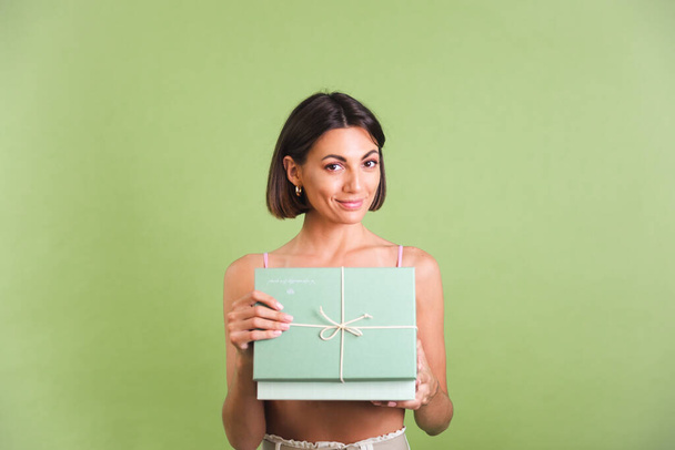Woman in pink crop top and white trousers on green background holding gift box happy positive excited cheerful posing - 写真・画像