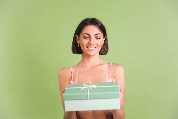 Donna in rosa crop top e pantaloni bianchi su sfondo verde contenente scatola regalo felice positivo eccitato posa allegra - Foto, immagini