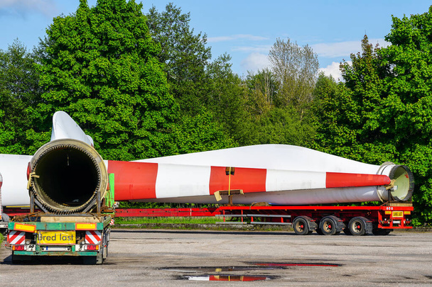 Una vista de un camión, un semirremolque de carga baja con piezas de turbina eólica de gran tamaño en el estacionamiento en el día de verano - Foto, imagen