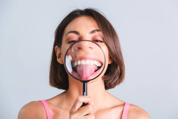 Pretty woman on gray background held magnifier happy shows her tongue - Photo, Image