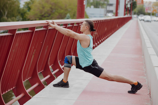 Man stretches leg before running on a bridge - Photo, image