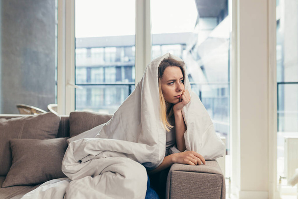 Portrait young woman sitting on sofa at home depressed. Girl is having a hard time with stress. Caucasian female indoors alone worried about problems. unhappy blonde student in living room or bedroom - Foto, immagini