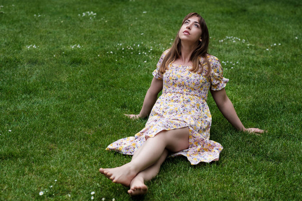 Relaxed young woman sitting on the grass in a spring day. She is wearing a spring dress. - Photo, Image