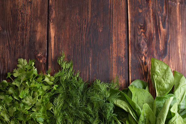 Side of bunches of greens: spinach, dill, cilantro, parsley on a wooden background, copy space, raw food concept, close up. - Photo, Image