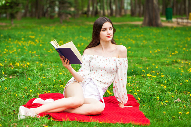 Young beautiful girl with a book resting in a summer park - Photo, Image