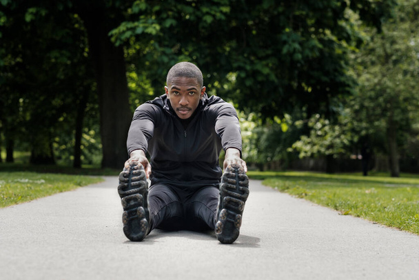 Portret czarnego sportowca rozciągającego się w parku. Ma na sobie czarny, aktywny strój.. - Zdjęcie, obraz