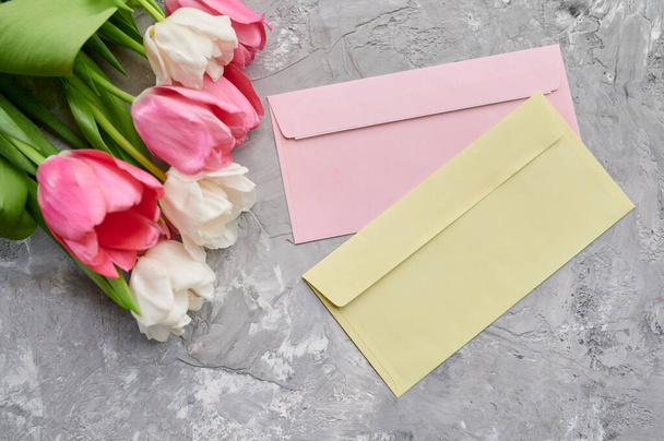Tulips and envelopes on grunge grey background. Spring flowers blooming, fresh floral decoration for greeting, green freshness, romantic gift - Photo, Image