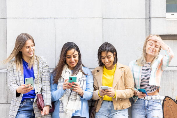 Grupo multiétnico de belas jovens amigas em pé contra uma parede usando smartphones móveis - Foto, Imagem