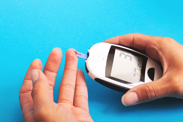 Blood glucose meter in hand on blue background close up - Foto, immagini