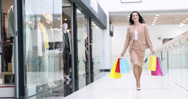 Gelukkig glimlachende vrouw wandelen in winkelcentrum met veel veelkleurige tassen in haar handen 4k film - Video