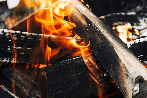 Vuur in het bos. Close-up van laaiend kampvuur, kampvuur branden logs in grote oranje en gele vlammen in close-up van het hout in brand. Hete open haard met vlammen en gloeiende ember - Foto, afbeelding