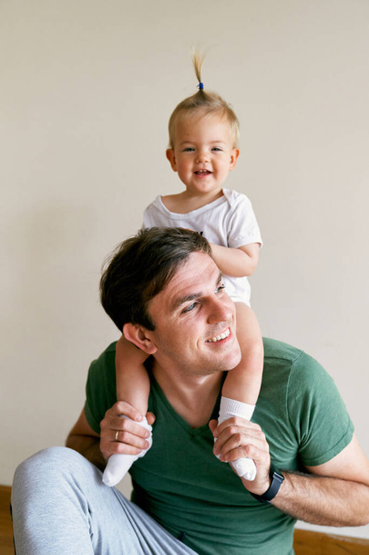 Glimlachende vader met een klein meisje op zijn schouders - Foto, afbeelding